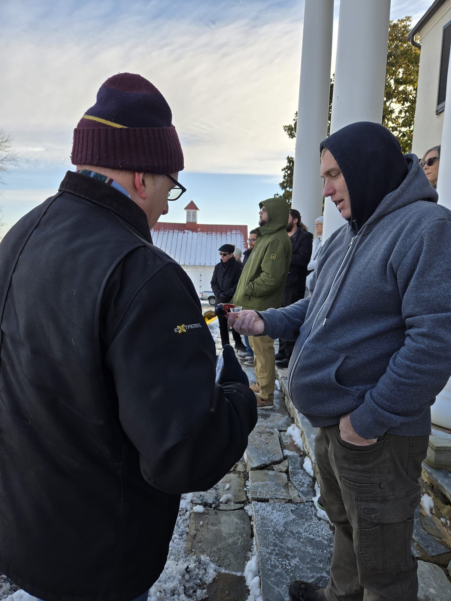 A handsome guy pouring whisky for a gentleman in a gray hoodie.